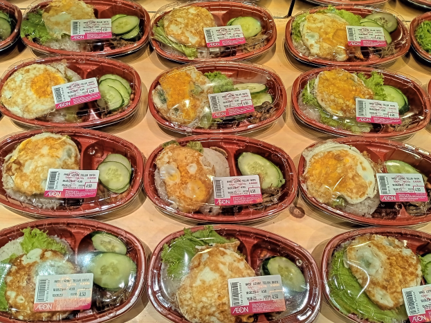 Eine Vitrine voller verschiedener Lebensmittel in Plastikbehältern, jeweils mit einem Preisschild, darunter Salate, Sandwiches und andere Gerichte.