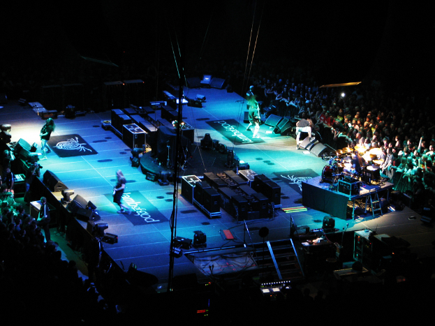 Eine Bühne mit Performern, Equipment und einer großen Zuschauermenge auf beiden Seiten vor einem dunklen Hintergrund.