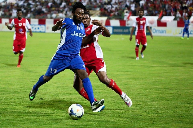 Eine Gruppe von Männern, die Fußball auf einem Feld spielen, tragen Benfica-Trikots, mit Zuschauern und Werbetafeln im Hintergrund.