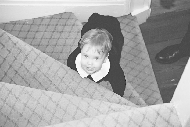 Ein Kind sitzt auf einer Treppe mit Schuhen, die rechts in einem Schwarz-Weiß-Bild angeordnet sind.