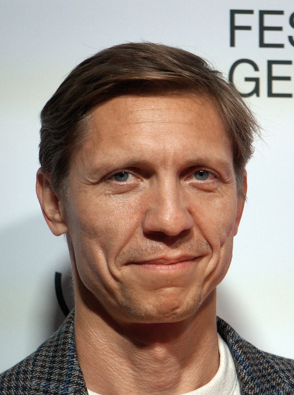 Ein Mann im Anzug und Krawatte lächelt in die Kamera, während im Hintergrund eine Tafel mit der Aufschrift "Eddie Redmayne Net Worth" zu sehen ist.