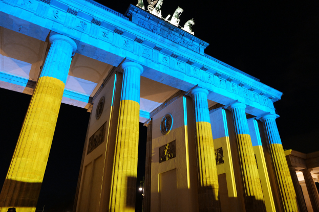 Das Brandenburger Tor in Berlin, Deutschland, erleuchtet in Blau und Gelb, mit Skulpturen gegen einen dunklen Hintergrund.