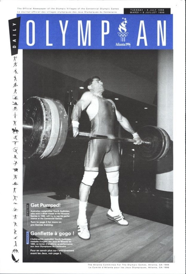 Schwarzes und weißes Foto eines Mannes in einem Kraftsport-Outfit, der eine Hantel stemmt, mit dem Text "Olympian Magazine" oben und einem entschlossenen Gesichtsausdruck.