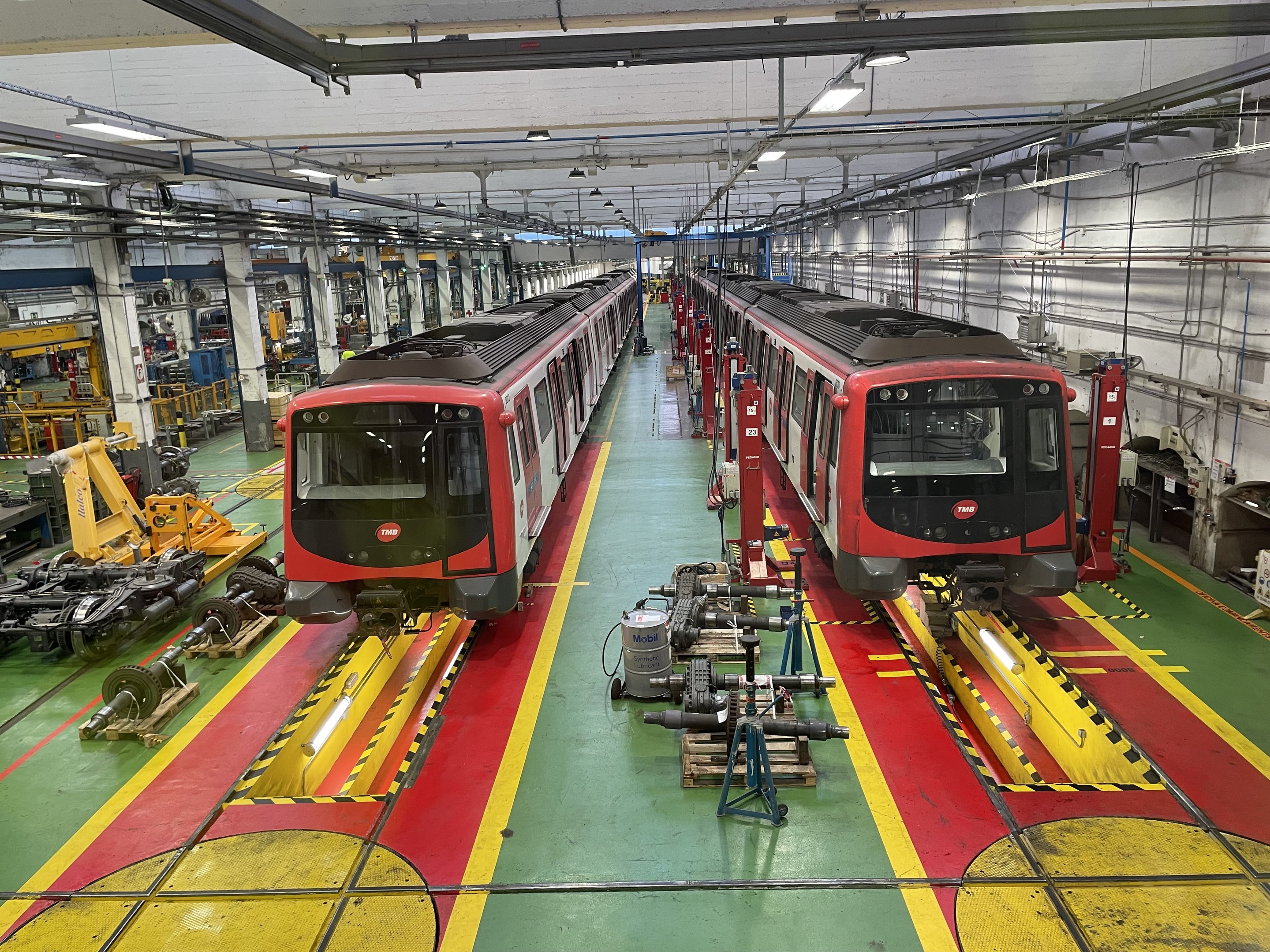 Zwei Züge auf den Schienen in einer großen Industriehalle mit Maschinen und Equipment, mit einer Wand mit Rohren und Deckenleuchten auf der rechten Seite, Teil der Daimler Group's Einrichtung.