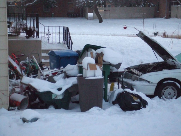 Eine Au√üenszene mit M√ľll in der Mitte, ein Auto rechts, Treppen links, B√§ume oben und Eis am Boden.