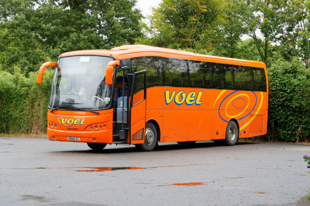 Ein Bus fährt auf einer Straße mit Bäumen und Himmel im Hintergrund.