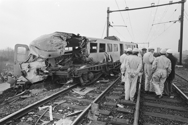 Ein Schwarz-Weiß-Bild einer Zugkollision auf den Schienen mit Einsatzkräften in Helmen und sichtbarer Infrastruktur.