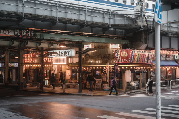 Eine Gruppe von Menschen √∞ber die Stra√Ÿe neben einem Zug gehend, mit einem Schild im Vordergrund und einer Br√∞cke mit einem Zug im Hintergrund.