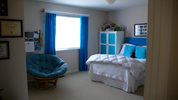 Ein Raum mit einem Bett, einem Stuhl, einem Fenster mit Vorhängen, einem Schrank, einem Fotorahmen und einem gefliesten Boden.