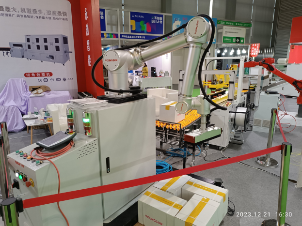 Eine Gruppe von Robotern auf einem Tisch umgeben von industrieller Ausrüstung, Bändern, Texttafeln und Beleuchtung, mit einer Person im Hintergrund und Unternehmenstext unten.