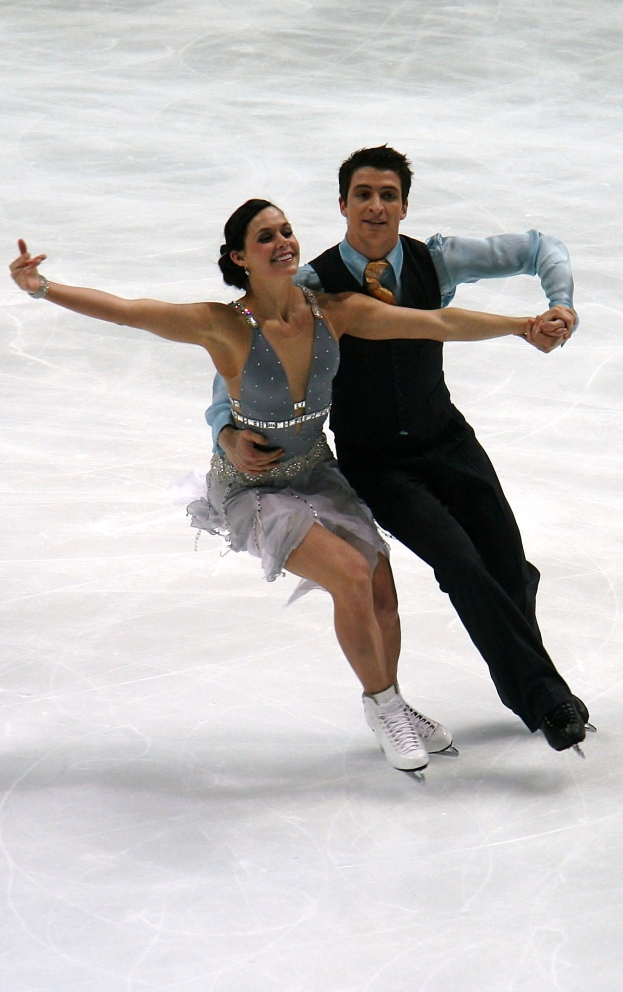 Eiskunstläufer Tessa Virtue in einem weißen Kleid und Scott Moir in einem schwarzen Anzug gleiten perfekt synchronisiert über glänzendes Eis.