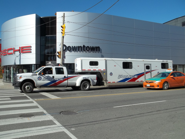 Polizeilaster vor einem Gebäude mit Text geparkt, mit einer Ampel und Leitungen im Vordergrund, Bäume und einen klaren blauen Himmel im Hintergrund.