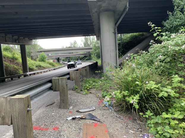 Auto unter einer Brücke mit Trümmern am Straßenrand, umgeben von Bäumen und einem klaren Himmel, wahrscheinlich nach einem tödlichen Crash auf dem I-95.