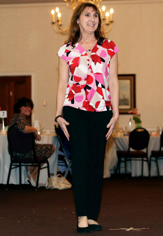 Eine Frau vor einem Bild an der Wand stehend, die lächelt, mit einer anderen Frau auf einem Stuhl neben einem Tisch mit einer Vase.