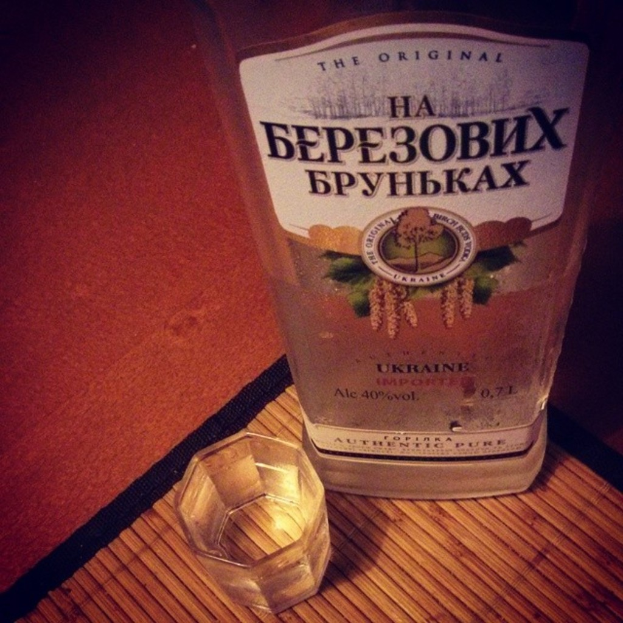 Ein klares Glas mit einer goldenen Flüssigkeit, wahrscheinlich Alkohol, auf einer dunklen, strukturierten Unterlage.