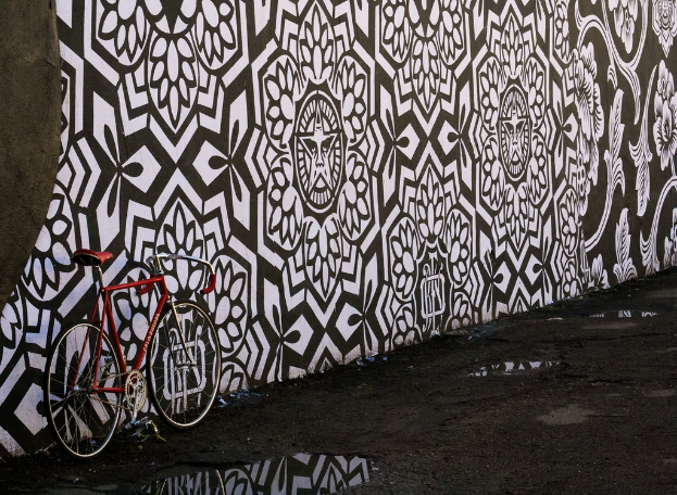 Eine Straße mit einem geparkten Fahrrad auf der linken Seite, einer bemalten Wand in der Mitte und einer Außenkulisse.