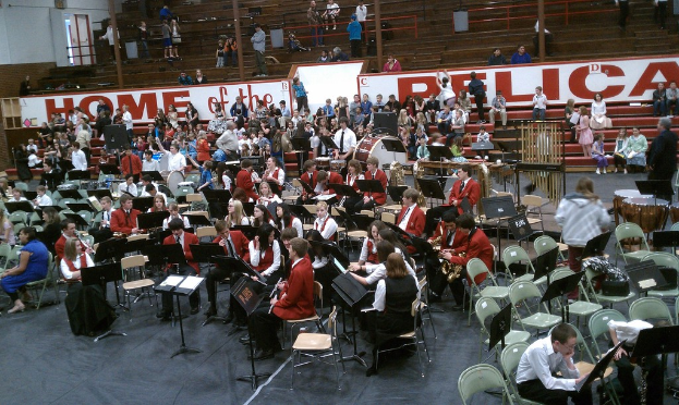 Eine Gruppe von Kindern sitzt auf Stühlen in einem Stadion während eines Musikunterrichts, wobei Stadionplätze im Hintergrund sichtbar sind.