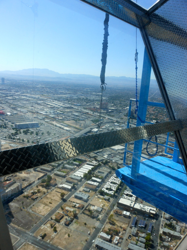 Eine Luftaufnahme einer Stadt mit Häusern, Bäumen, einer Fußgängerbrücke auf der linken Seite, fernen Hügeln und einem klaren Himmel.