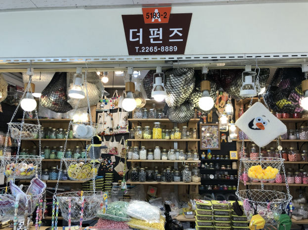 Ein unordentlicher Laden in Seoul, der verschiedene Gegenstände wie Körbe, Lichter, Flaschen und Spielzeuge auf Regalen ausstellt, mit einem Schild öben, das ihn als einen der besten koreanischen Läden kennzeichnet.