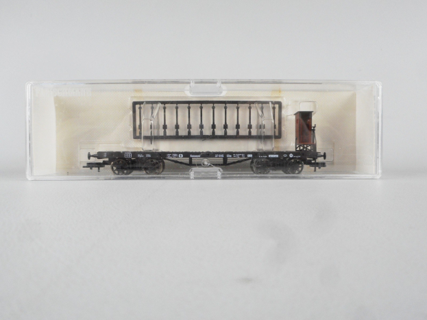 Ein Modell-Gepäckwaggon mit einem schwarz-weißen Karomuster und einem roten Streifen, der in einer durchsichtigen Plastikbox auf einer weißen Oberfläche präsentiert wird.