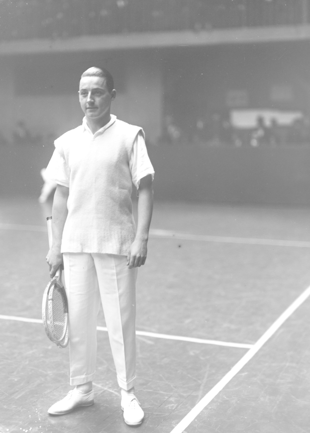 Ein Mann in einem wei├čem Tennisoutfit steht auf einem Tennisplatz und h├Ąlt einen Schl├Ąger mit entschlossener Miene, mit einem unscharfen Hintergrund.