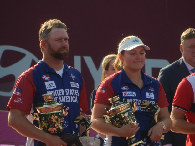 Gruppe von Menschen, die Trophäen halten, mit dem Hintergrund 'Weltarcherie-Meisterschaften'.
