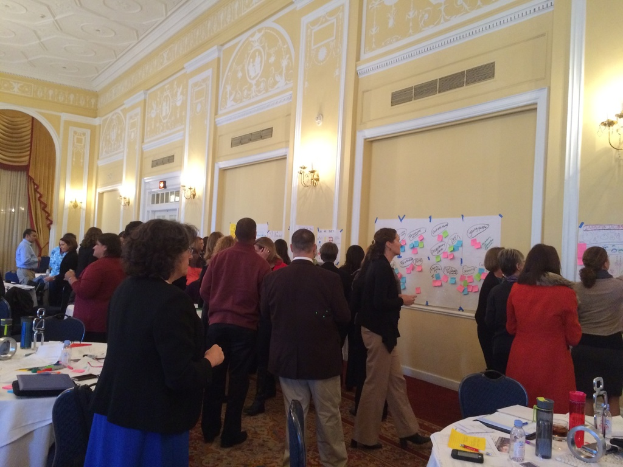 Eine Gruppe von Menschen, die Plakate und Diagramme auf einer Wand in einem scheinbar Kunstmuseum betrachtet.