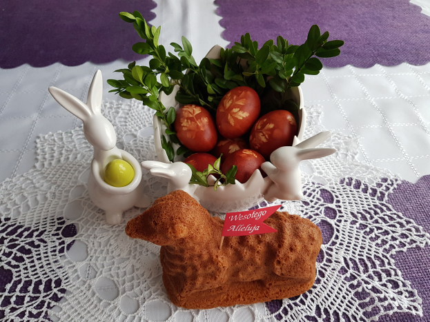 Ein mit einer Decke drapierter Tisch hält eine Schüssel mit bunten Ostereiern mit Osterhasen-Figuren darauf.