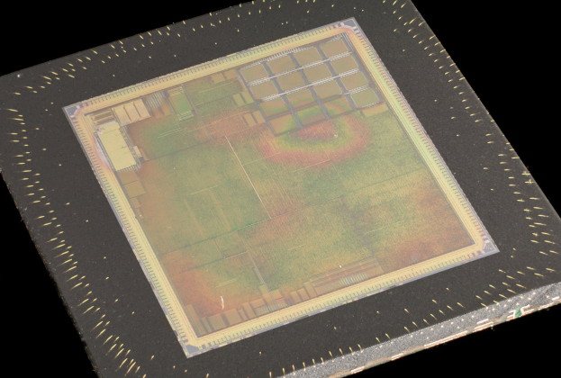 Nahaufnahme eines rechteckigen Halbleiterchips mit metallischem Glanz, schmalem Metallrahmen und kleinen Kantenl├Âchern auf schwarzem Hintergrund, mit leicht erh├Âhten Kanten.