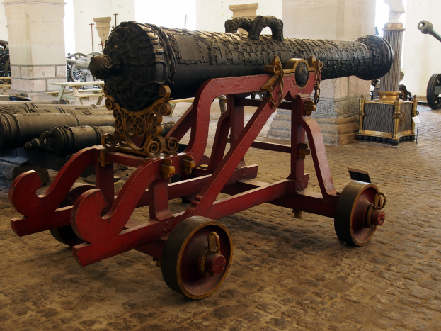 Ein altes Geschütz in einem Museum ausgestellt, umgeben von anderen Geschützen und Säulen.